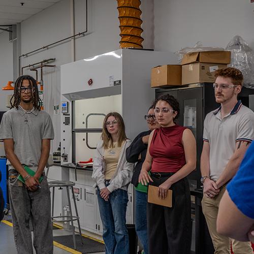 Iona University students wearing safety glasses while listening to a speaker inside a research and development laboratory at Eos Energy Enterprises.