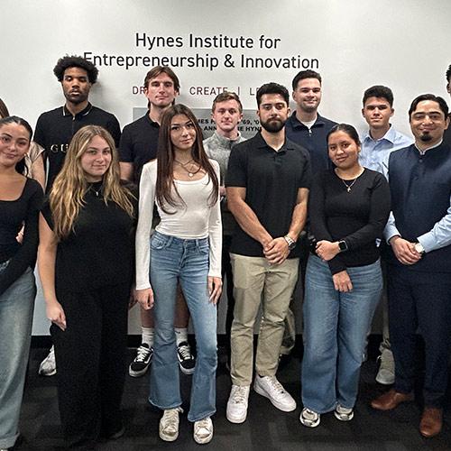 A group of Iona University students and faculty pose for a photo in front of the Hynes Institute for Entrepreneurship & Innovation sign.