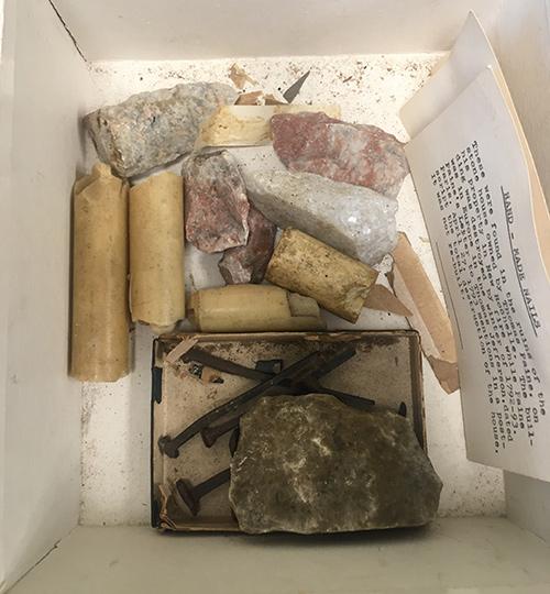 The ITPS Lord and Taylor box that contains nails that were once part of Paine’s home in New Rochelle, some used candles, some pieces of paper, and several rocks.