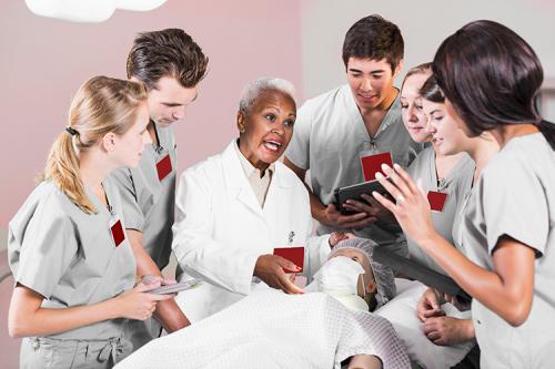 A nursing professor instructs a group of nursing students using an artificial patient doll.