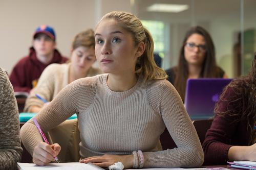 A student sits in class attentively with her pen poised ready to take notes.