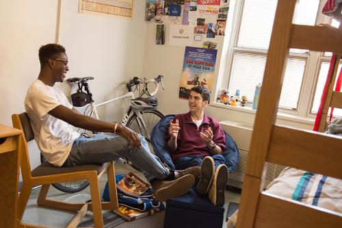 Two students smile and have a conversation in a Living Learning Community dorm room.