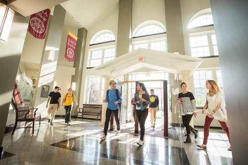 Students enter Ryan Library as beautiful sunlight shines through the glass doors and windows.