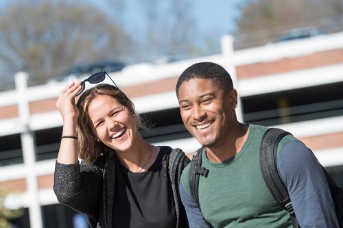 Two graduate students smile and laugh near the parking garage on campus.