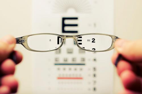 A pair of glasses is held in front of a chart used for eyesight exams.