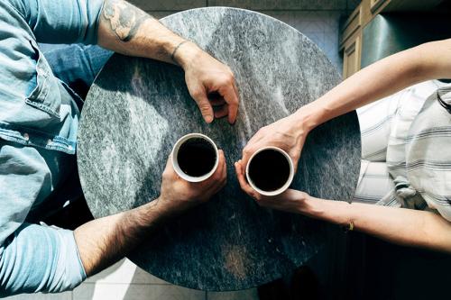 Two people hold cups of coffee on a table.