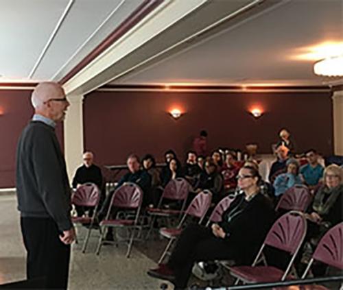 Brother Cawley stands in front of an audience in Burke Lounge.