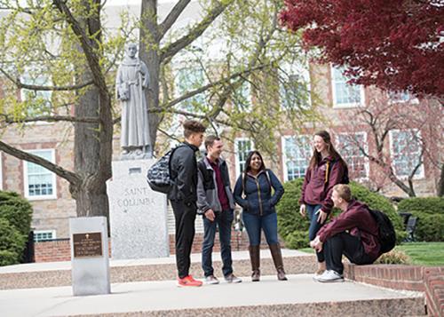 Students stand and talk together in front of the ginkgo tree.