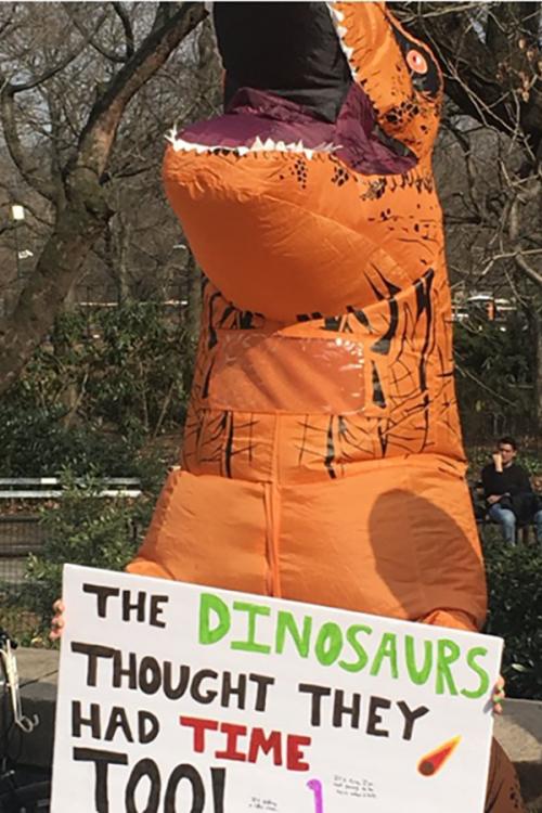 Someone in a dinosaur suit protests in support of climate change.