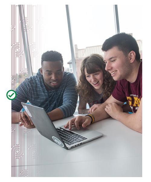 Three students sit together and look at a laptop screen. Celtic line art runs in a vertical orientation on the left hand size of the image.
