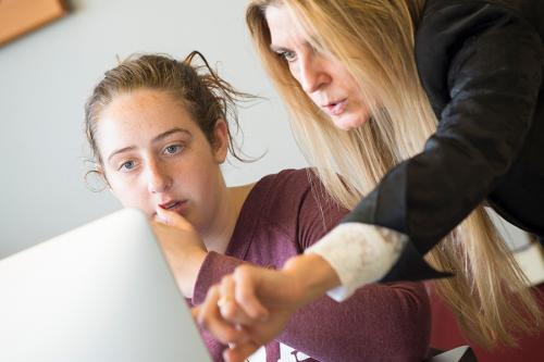 A student looks at a computer with a faculty member who is pointing at the screen.