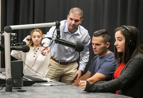 Joe from Media & Strategic Communication department shows three students how to use the podcast/radio equipment.