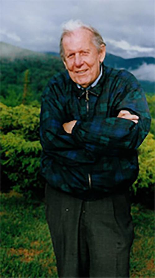 Thomas Berry in a green sweater in a field with a mountain in the background.