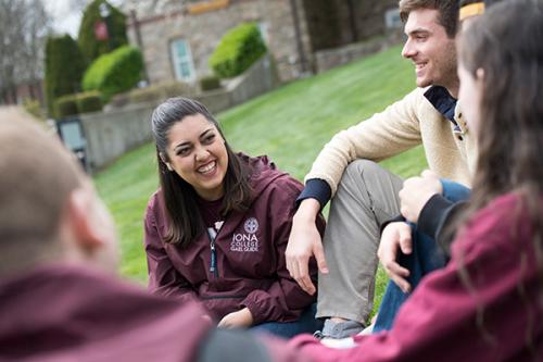 Students sit and talk on the east lawn. One student wears a Gael Guides jacket.