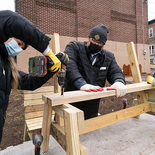 A student and Br. Ford drill a table together at the Fuller house.