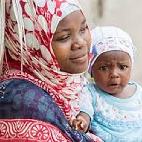 A woman in a red and white headdress holds her baby. 