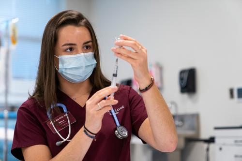A female nursing student practices filling a syringe with medication.