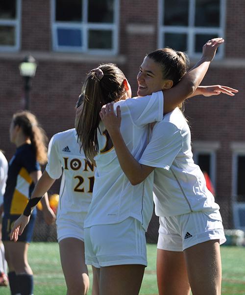 Two players hug and smile after a goal during women's soccer.