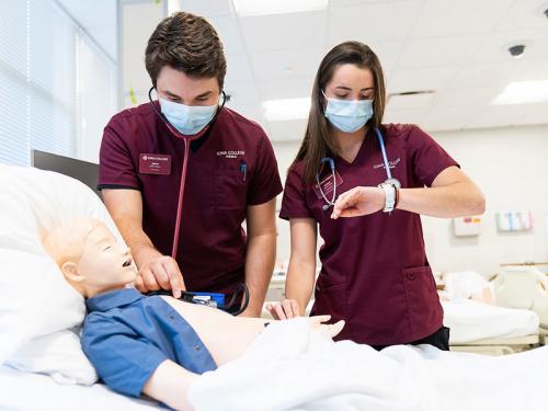 Two nursing students work on a mannequin patient.
