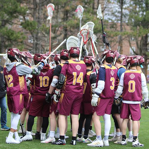 The Iona men's lacrosse club team huddle on field with their sticks raised in the air.