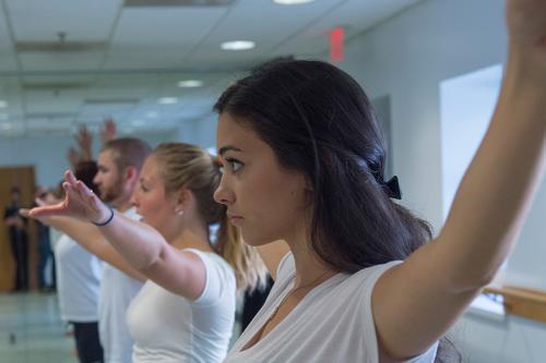 Dance students raise their arms in class.