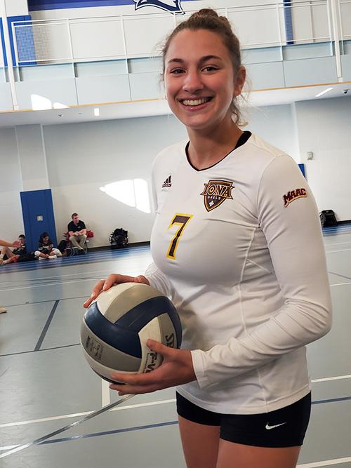 A club volleyball player holds the ball and smiles.