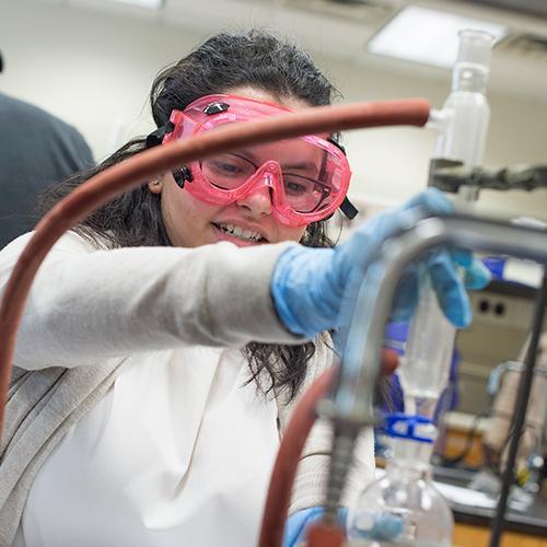 A student in pink goggles performs an experiment.