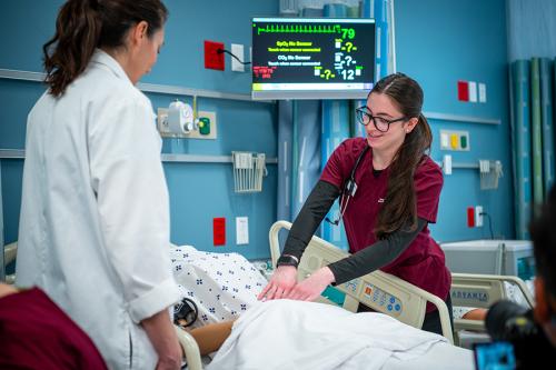A nursing student practices pressing against a mannequin's stomach.