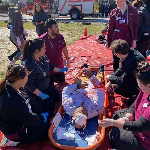 Students in the nursing simulation help someone in a stretcher.