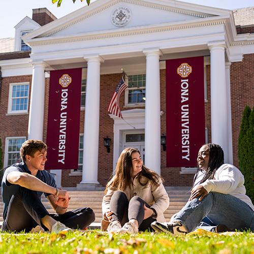 Three students sit outside of McSpedon Hall on a sunny day.