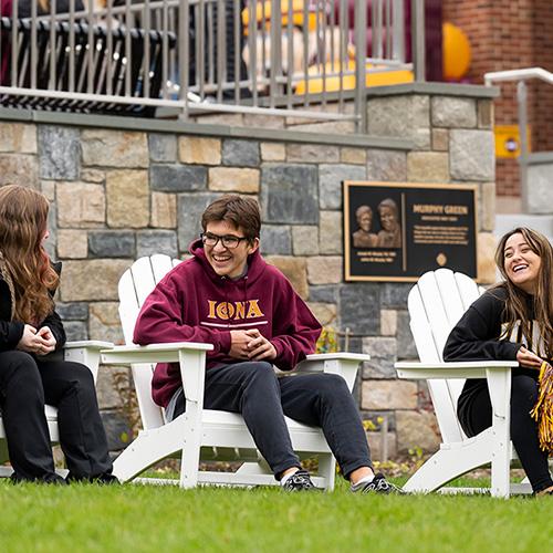 Three students sit on adironcack chairs on the Murphy Green.