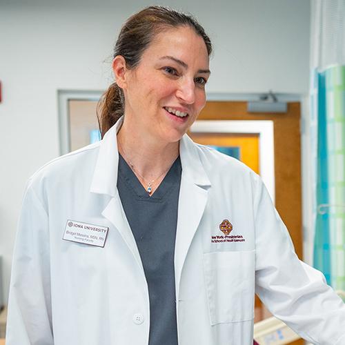 A nursing professor in a white lab coat smiles and helps a student.