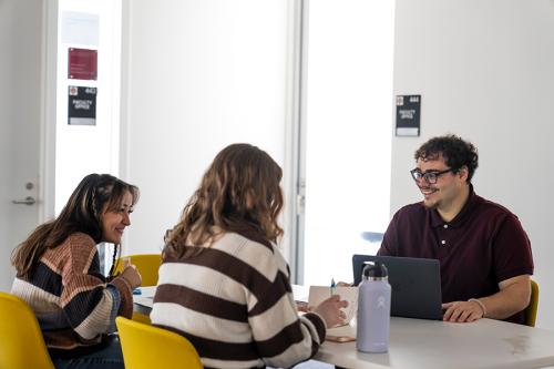 Three students smile and work together in the LaPenta School of Business.