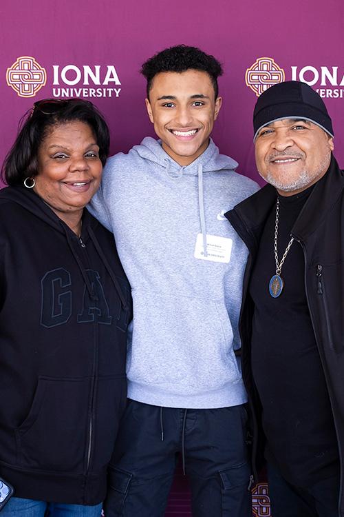 A student smiles with his parents in front of the step and repeat.