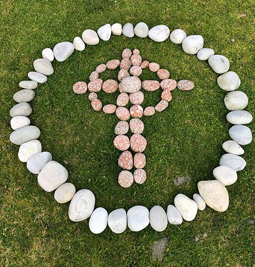 A stone design on grass making a Celtic Cross inside of a circle.