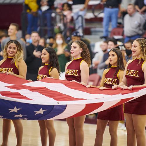 The Iona dance team holds an American flag at a basketball game.
