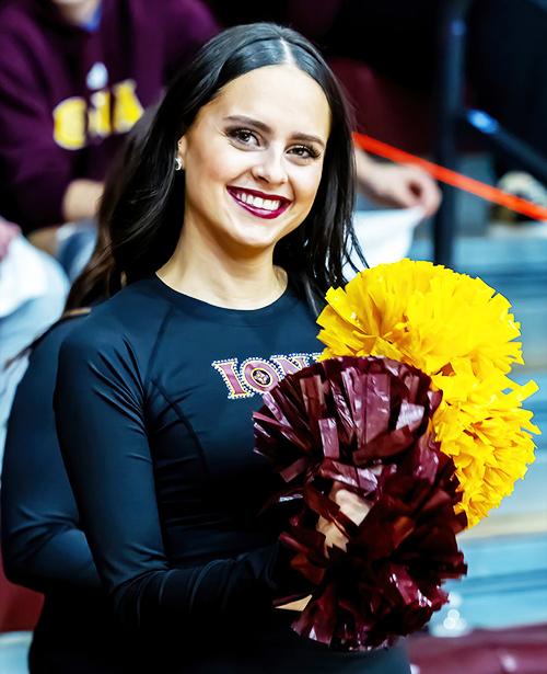 A member of the dance team smiles and holds her pom-poms.
