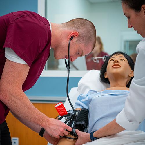 A nursing student works with a professor on a mannequin taking blood pressure readings.