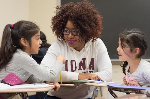A student teacher works with two young students on their reading.