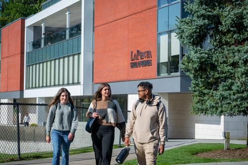 Three students walking by the LSB on a sunny day.