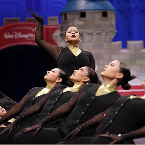 Iona Dance Team performing on stage in sync with each other expect for one dance member posing in the center of the dance routine.