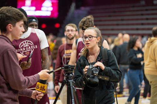 Students work at a basketball game shooting video and photos.