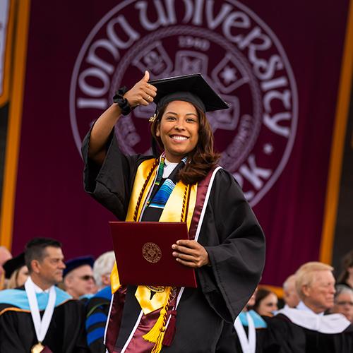 A graduate gives a "thumbs up" on stage at commencement.