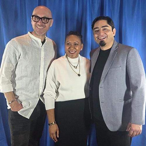 Dr. Christoph Winkler smiles alongside two colleagues while posing together in front of a blue draped backdrop.