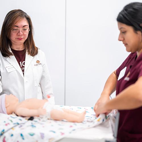 A nursing student and professor work with a mannequin baby.
