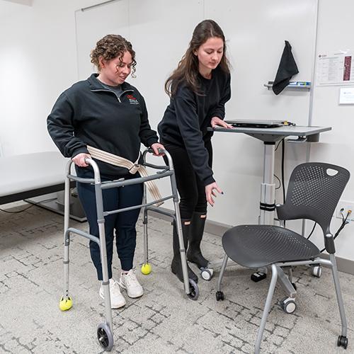 Two OT students practice helping a patient with a walker.