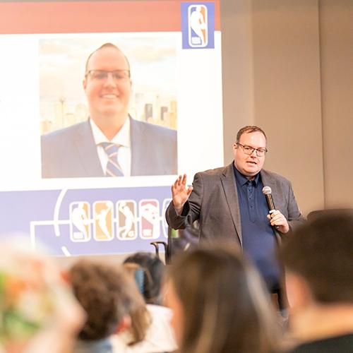Barney Carlton, NBA vice president of broadcast strategy, speaks to a crowd of students at Iona University’s Romita Auditorium with a presentation slide about team culture displayed behind him.