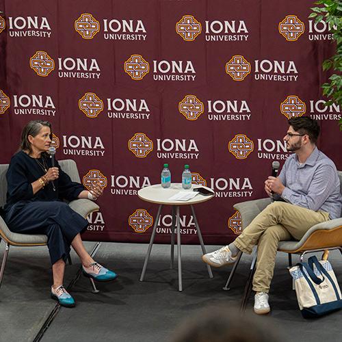 Amy Emmerich ’97 and Landon Popovic ’27 engage in a Q&A session on stage in front of an Iona University backdrop.