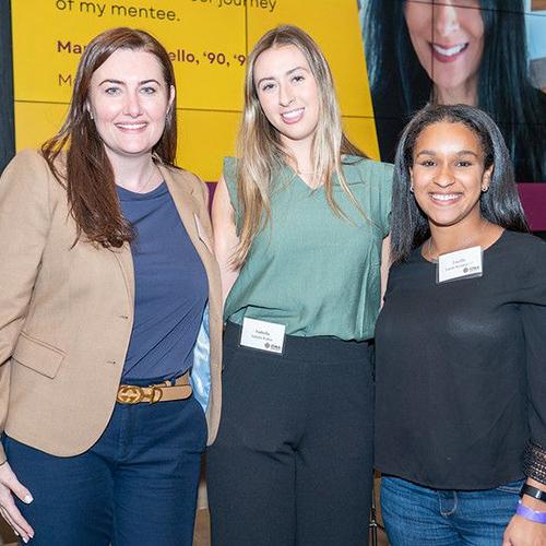 Lucille Bootman (right) smiles alongside two other women wearing name tags at an Iona University Gaels Go Further networking event, standing in front of a yellow digital display background.