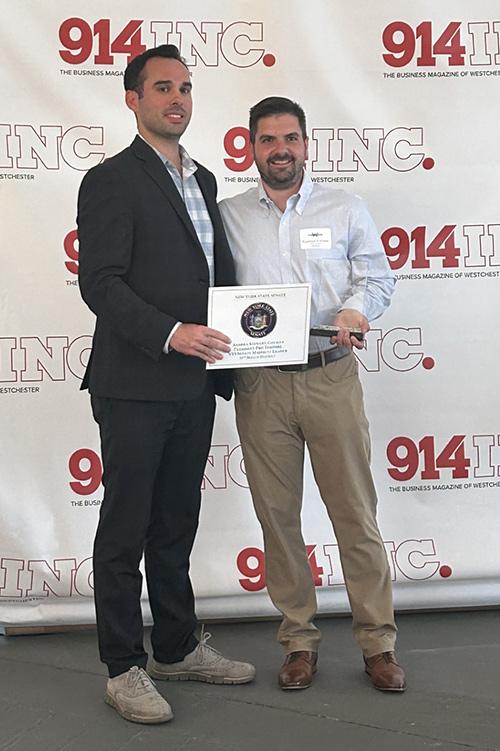 Giuseppe (Joe) D’Aloisio smiles with a colleague with the 914Inc. backdrop.